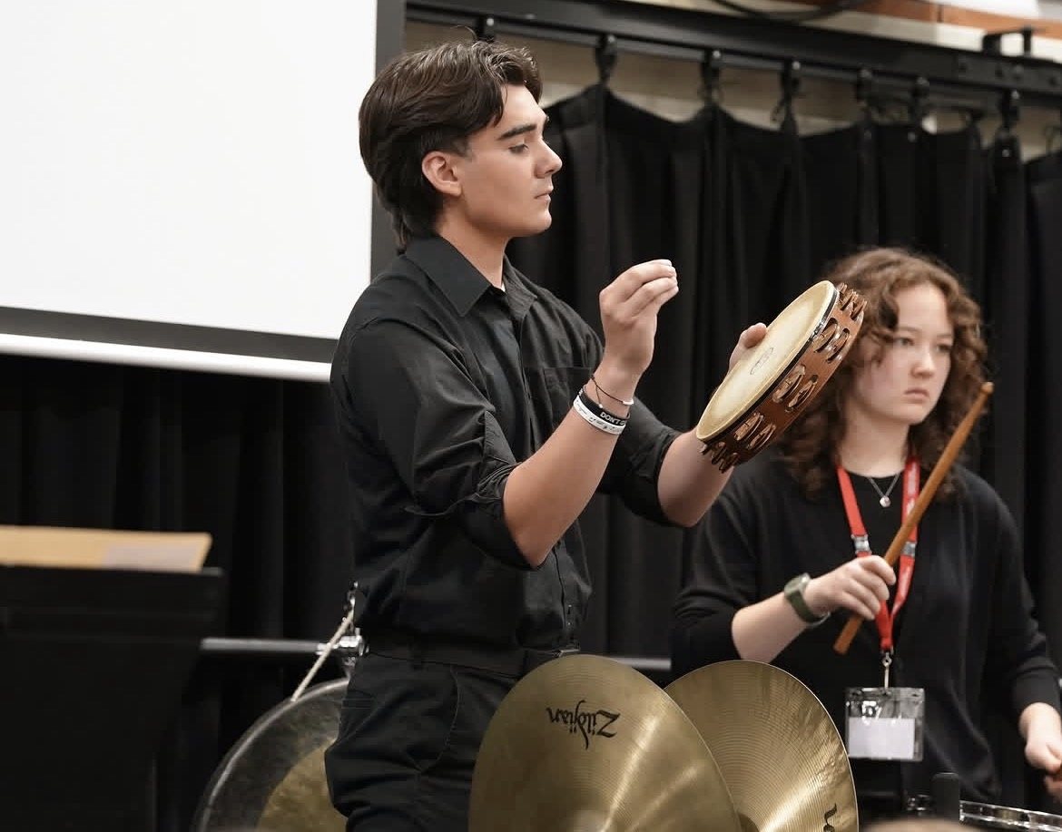 Makoa Lewis playing tambourine in rehearsal, with cymbals in the foreground